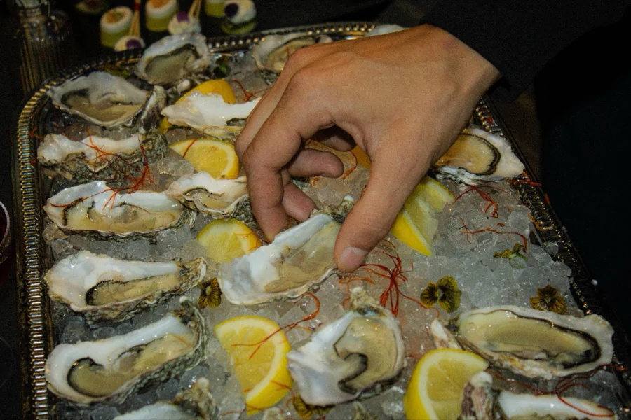 Une main attrape une huître sur un plateau de glace pilée et de citrons