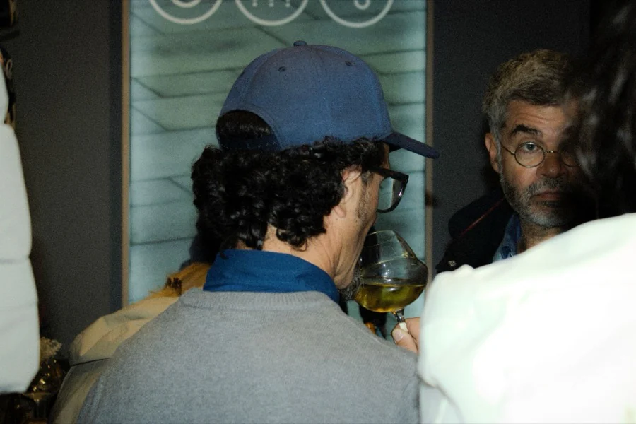 Un invité en casquette goûte le vin, face à un autre convive