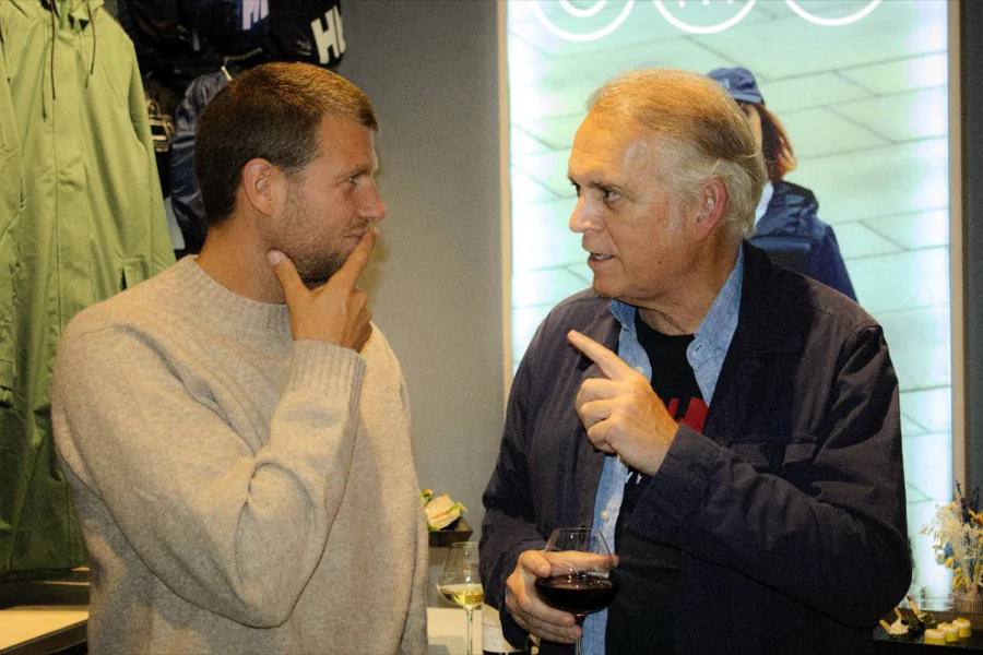 Deux invités discutent devant les vestes Helly Hansen, verre de vin rouge à la main