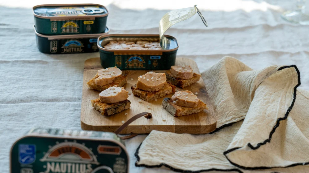 Toasts de foie de morue Nautilus et fleur de sel, boîtes de conserve en arrière-plan