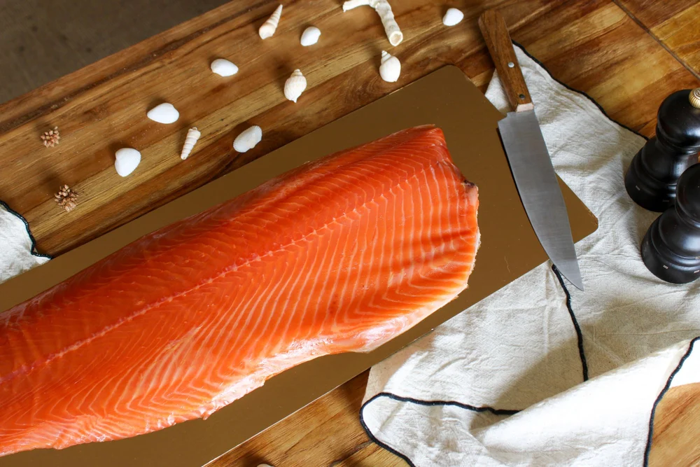 Filet de saumon fumé sur planche dorée, coquillages et couteau