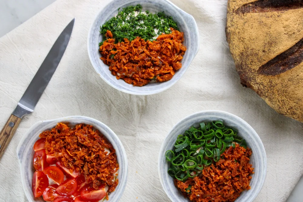 Trois bols de tartinades garnies d’éclats croustillants, d’aneth, de tomates et d’oignon nouveau