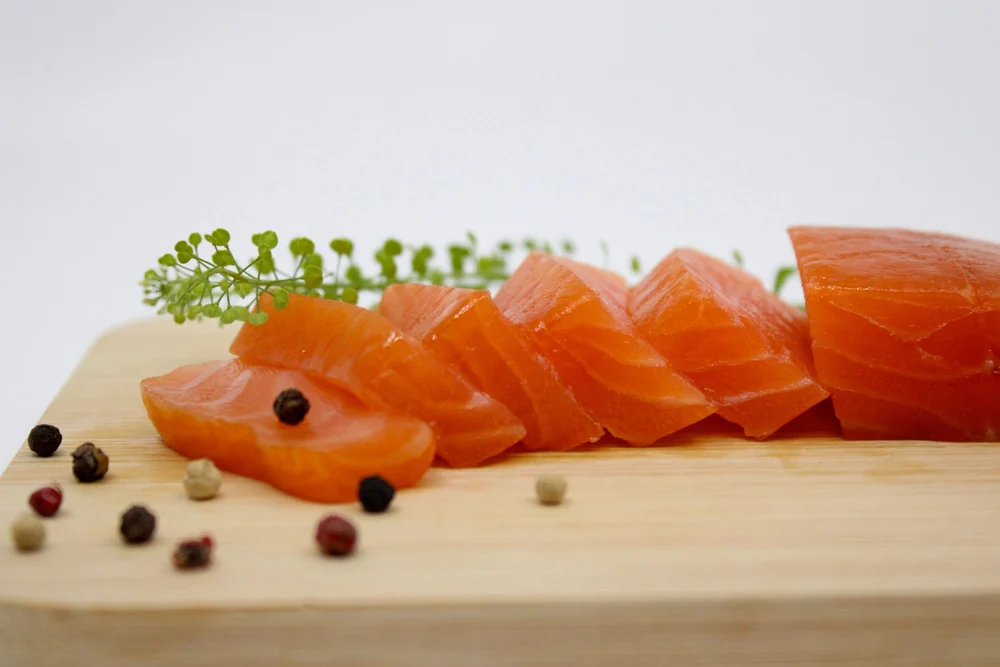 Morceaux de saumon fumé sur une planche, baies de poivre
